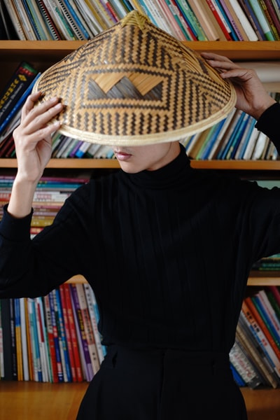 A woman dressed in a black long sleeved shirt and brown wicker cap
